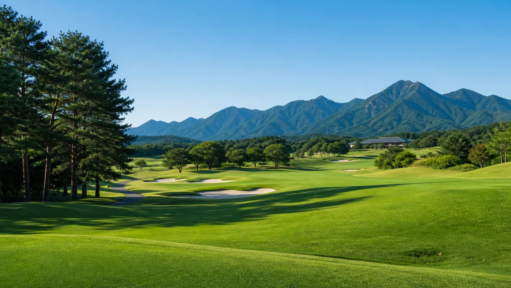 A sunlit Japanese golf course surrounded by mountains under a clear blue sky